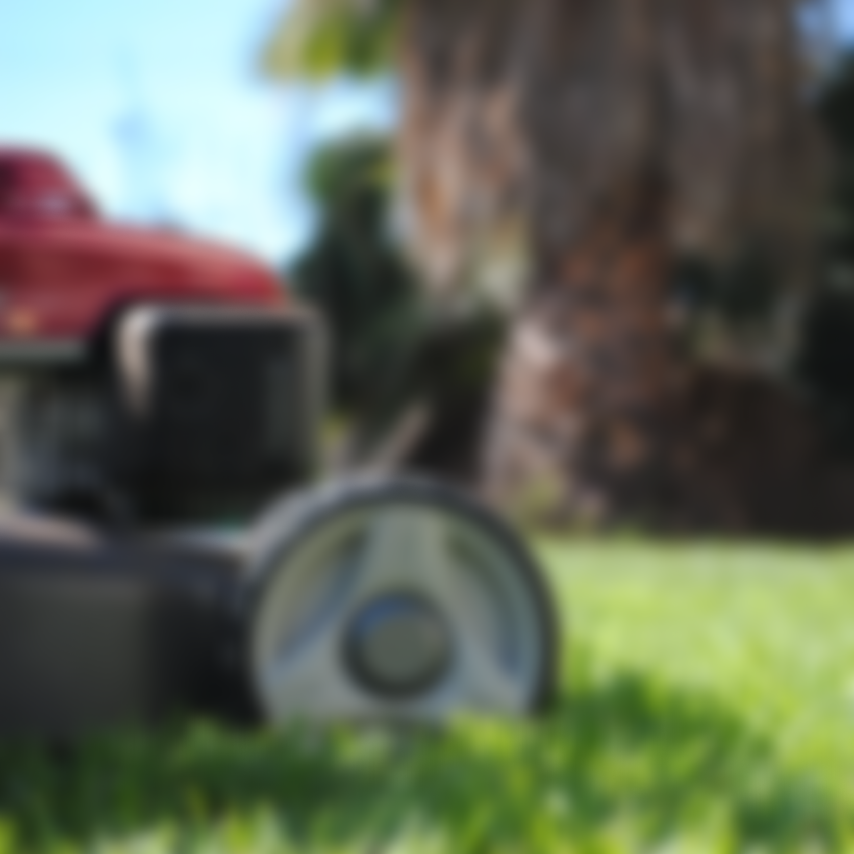 Blurred image showing a lawnmower outdoors on a lawn with, trees, and sky in the background.