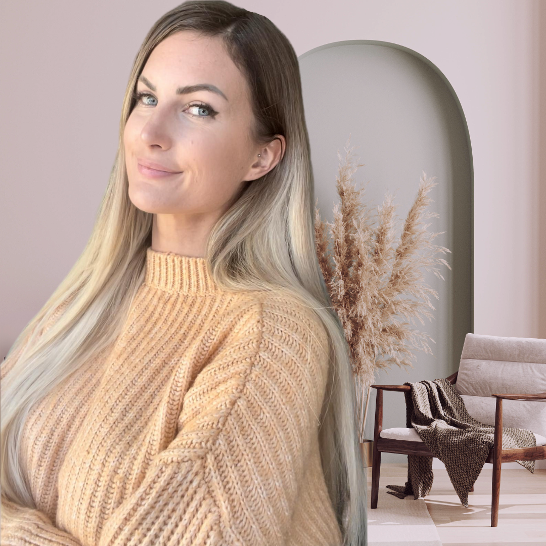 Une femme blonde souriante en pull beige dans un intérieur moderne avec un canapé, une plante sèche et une arche dans le mur.