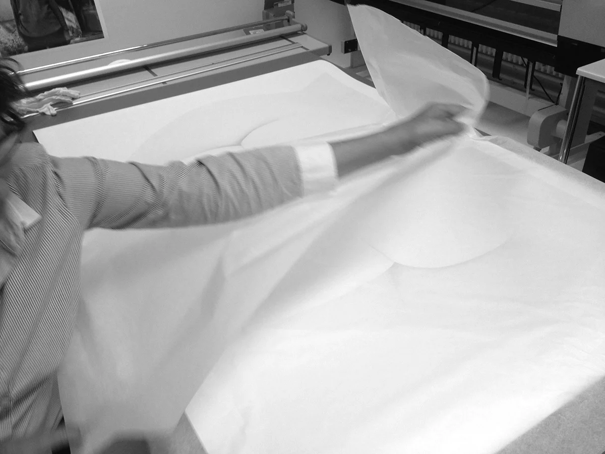 Hands lifting a sheet of thin archival paper from a large photographic print — preservation as a practice of care.