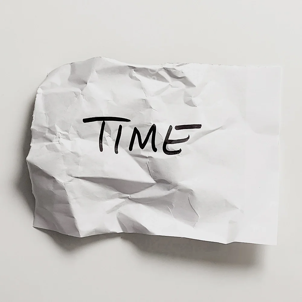 A crumpled white sheet of paper with the word "TIME" handwritten in black marker — Time made tangible, marked by lived experience.