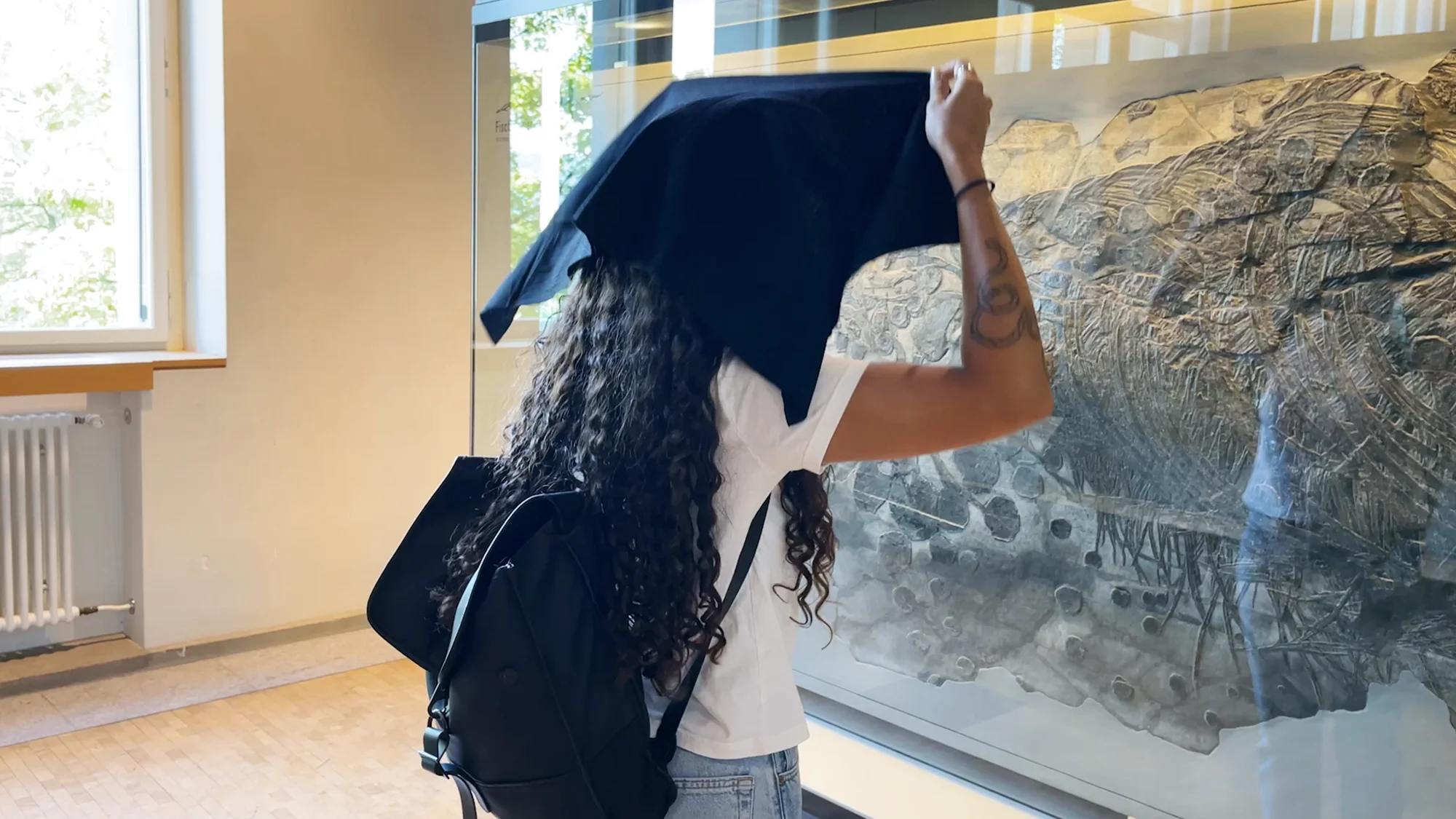 A museum visitor holds the Experience Enhancer over her head to study a detailed artwork — the instrument's black cloth narrowing seeing to a single object.