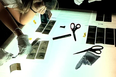 Two people at a light table inspect film negatives and sleeve them for archival storage — the physical results of a sustainable photography workshop.