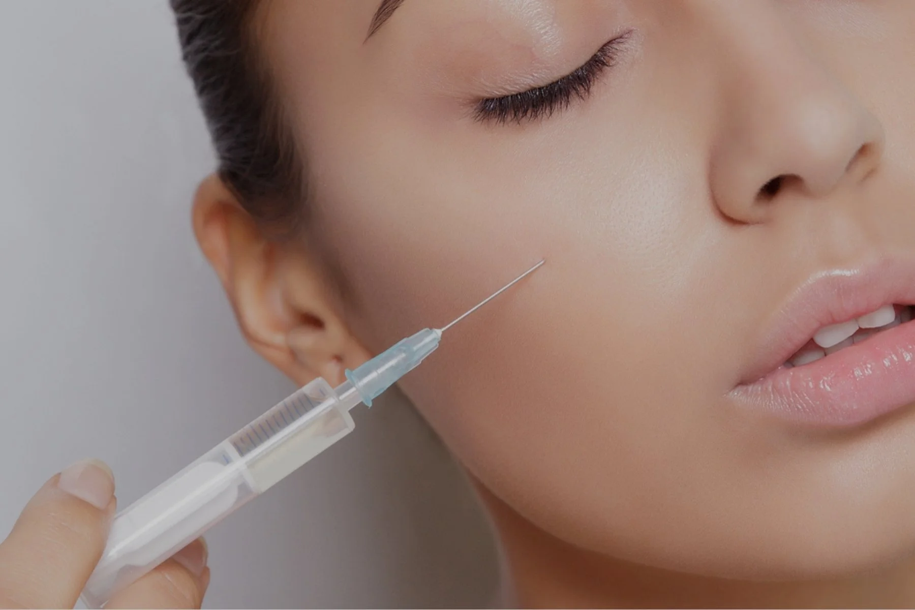A woman receiving a facial injection with a syringe held by a medical professional.