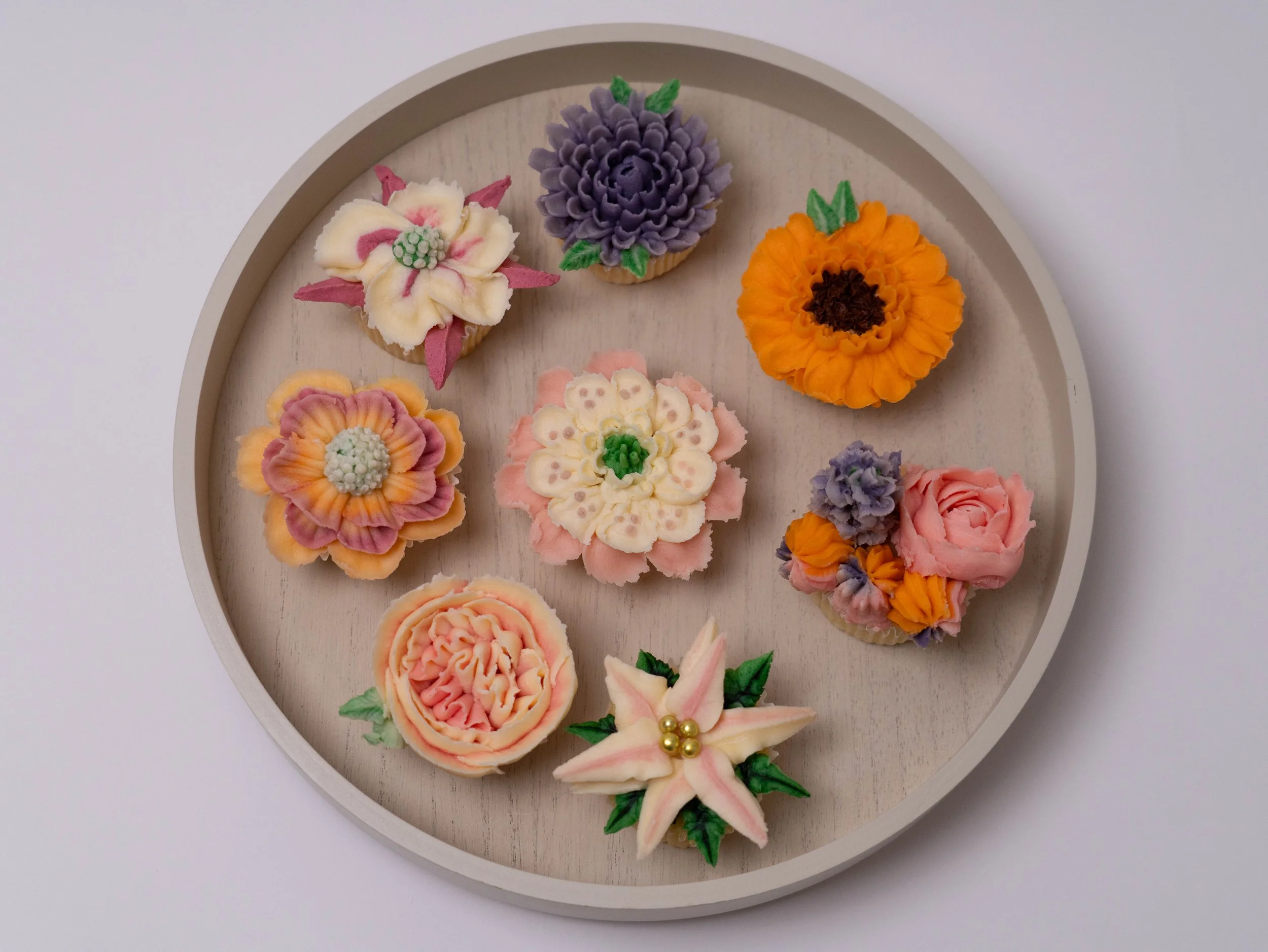 Assorted cupcakes decorated with floral designs on a round tray.