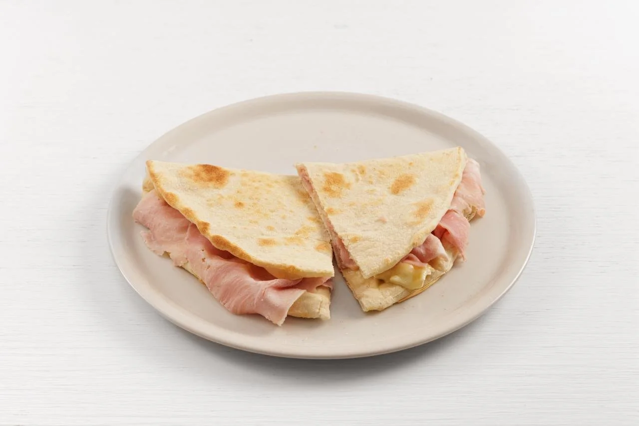 Sandwich di pane pita ripieno di prosciutto e formaggio, tagliato a metà, su un piatto bianco