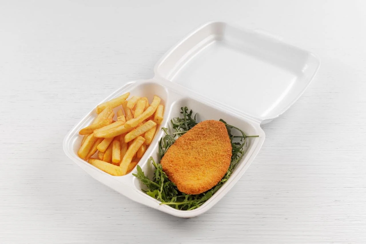 Contenitore porta cibo con patatine fritte e cotoletta impanata su foglie di insalata