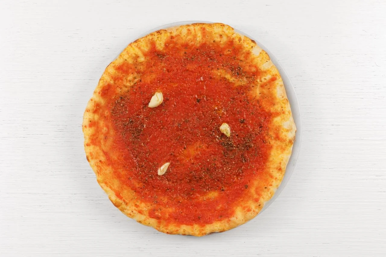 Pizza margherita con salsa di pomodoro, aglio, origano e basilico su una crosta sottile, vista dall'alto su sfondo bianco.