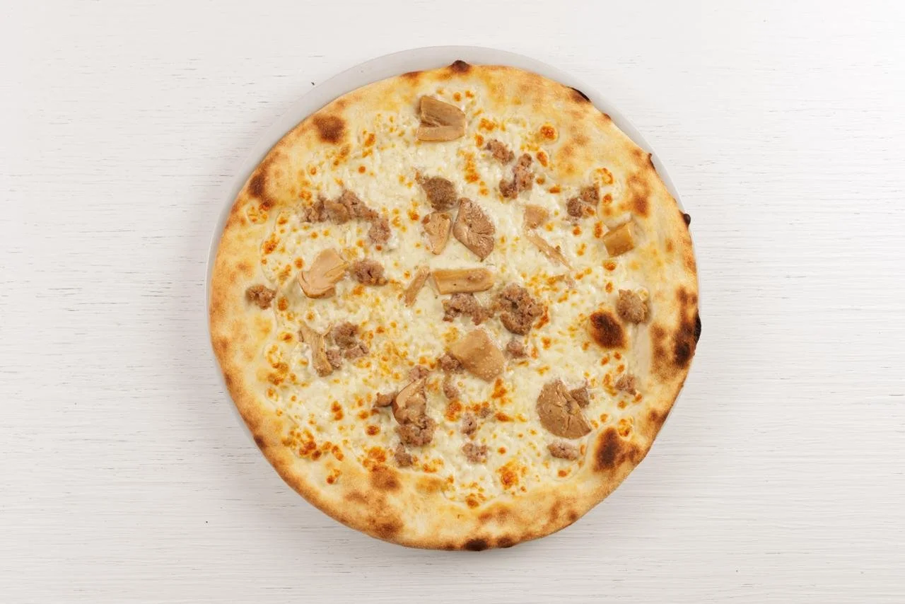 Pizza bianca con pollo e salsiccia su una superficie bianca