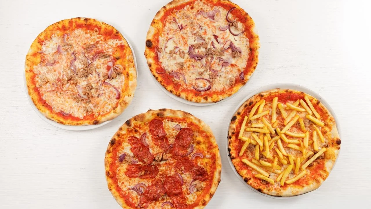 Quattro pizze con diversi condimenti su un tavolo bianco.