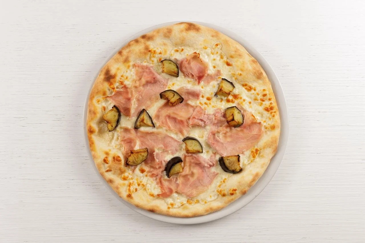 Pizza con prosciutto cotto e melanzane su piatto bianco