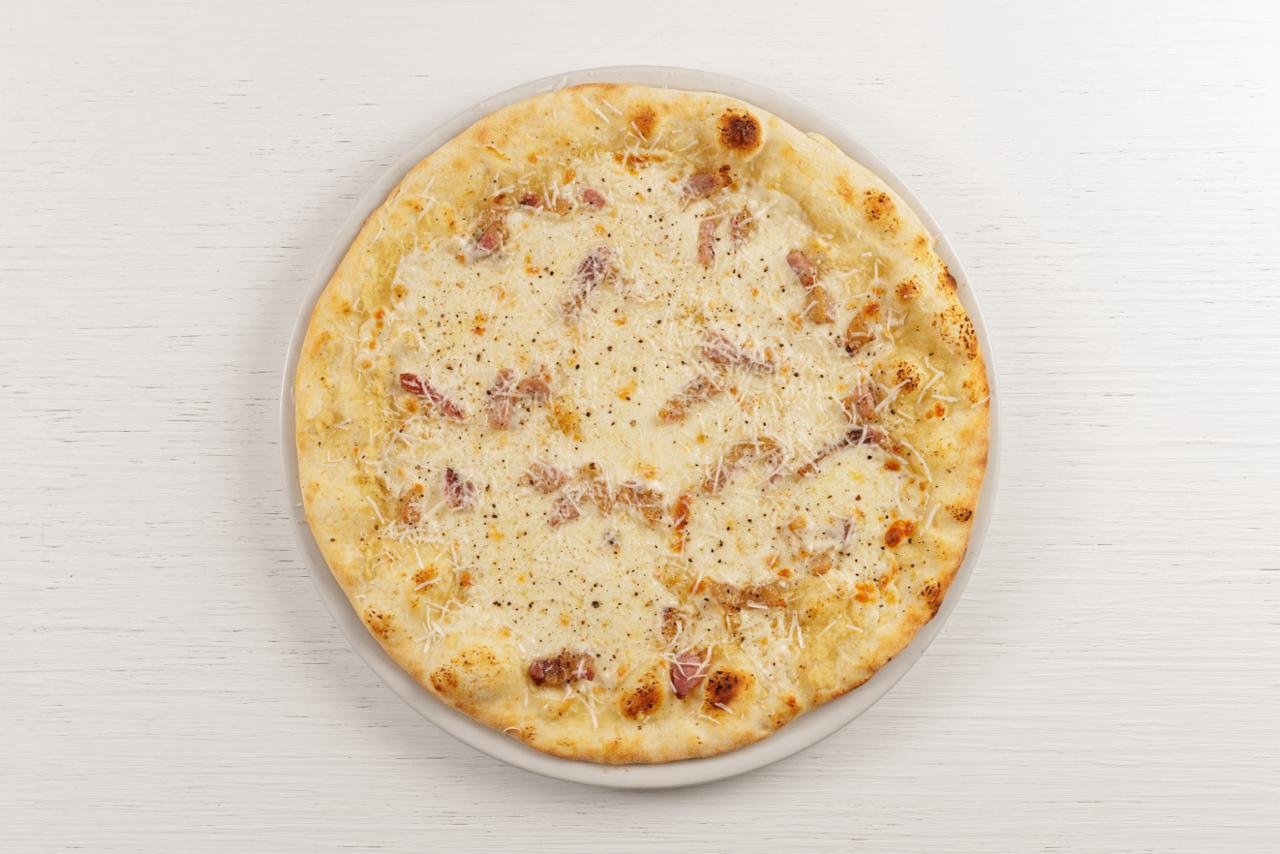 Pizza bianca con prosciutto e formaggio su piatto bianco.