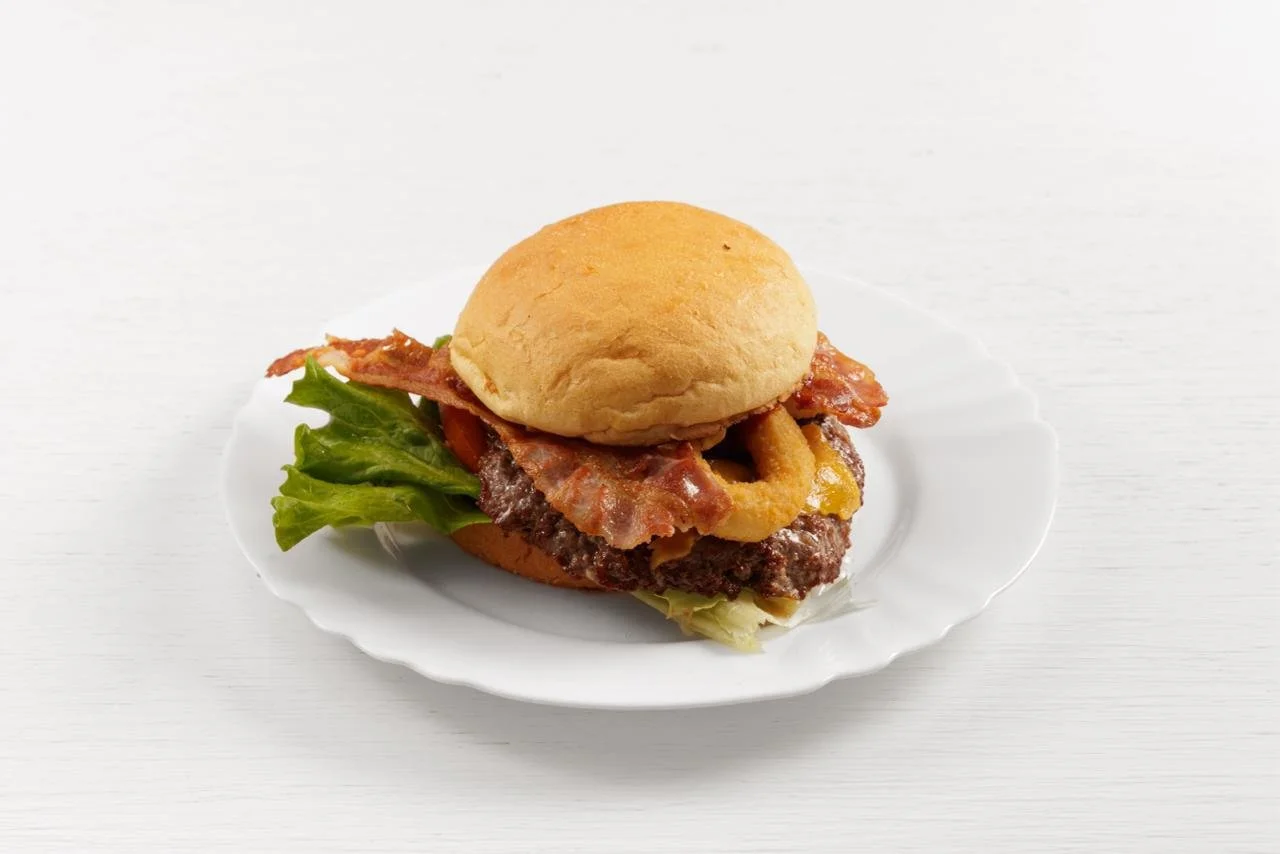 Panino con carne, bacon, cipolle e lattuga su piatto bianco.