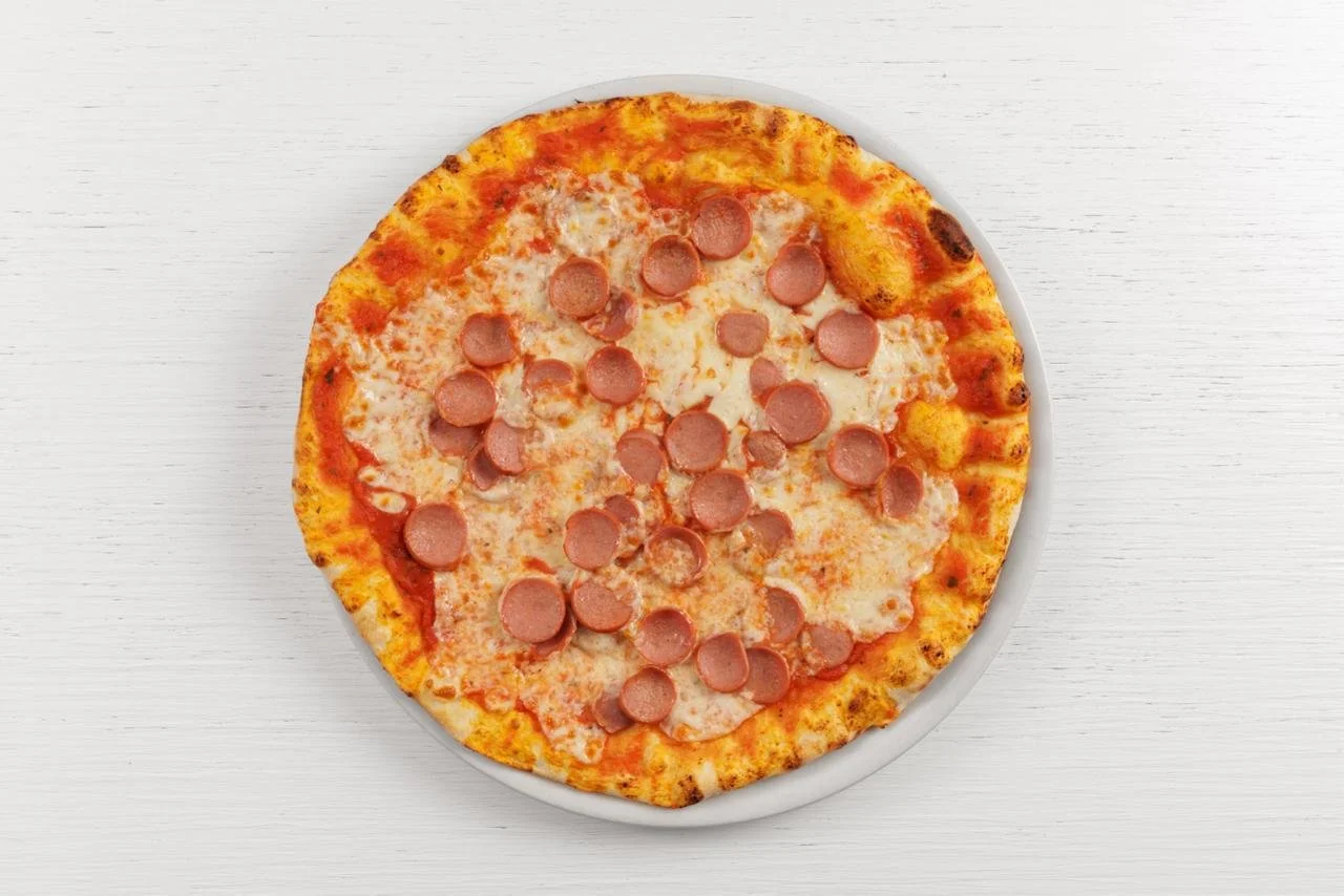 Pizza con pomodoro, formaggio e wurstel su un piatto bianco.