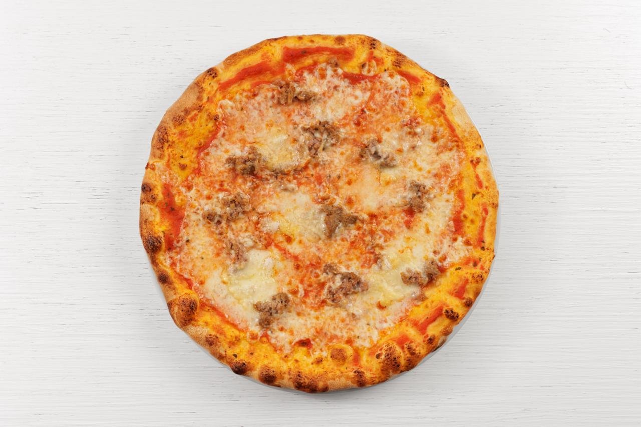 Pizza con pomodoro, formaggio e carne su un tavolo di legno chiaro.