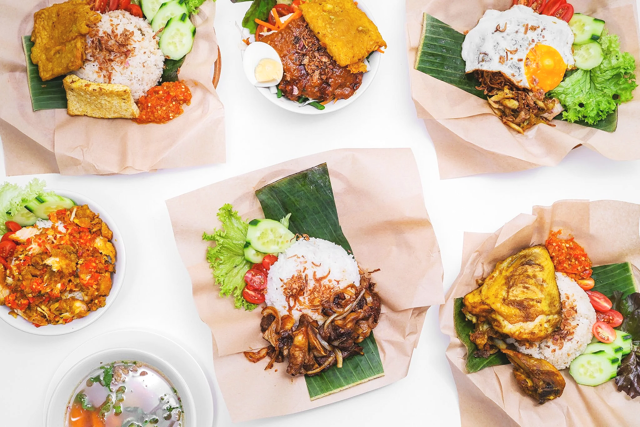 Various Indonesian dishes including rice with fried chicken, beef, and vegetables, served with chili and salad