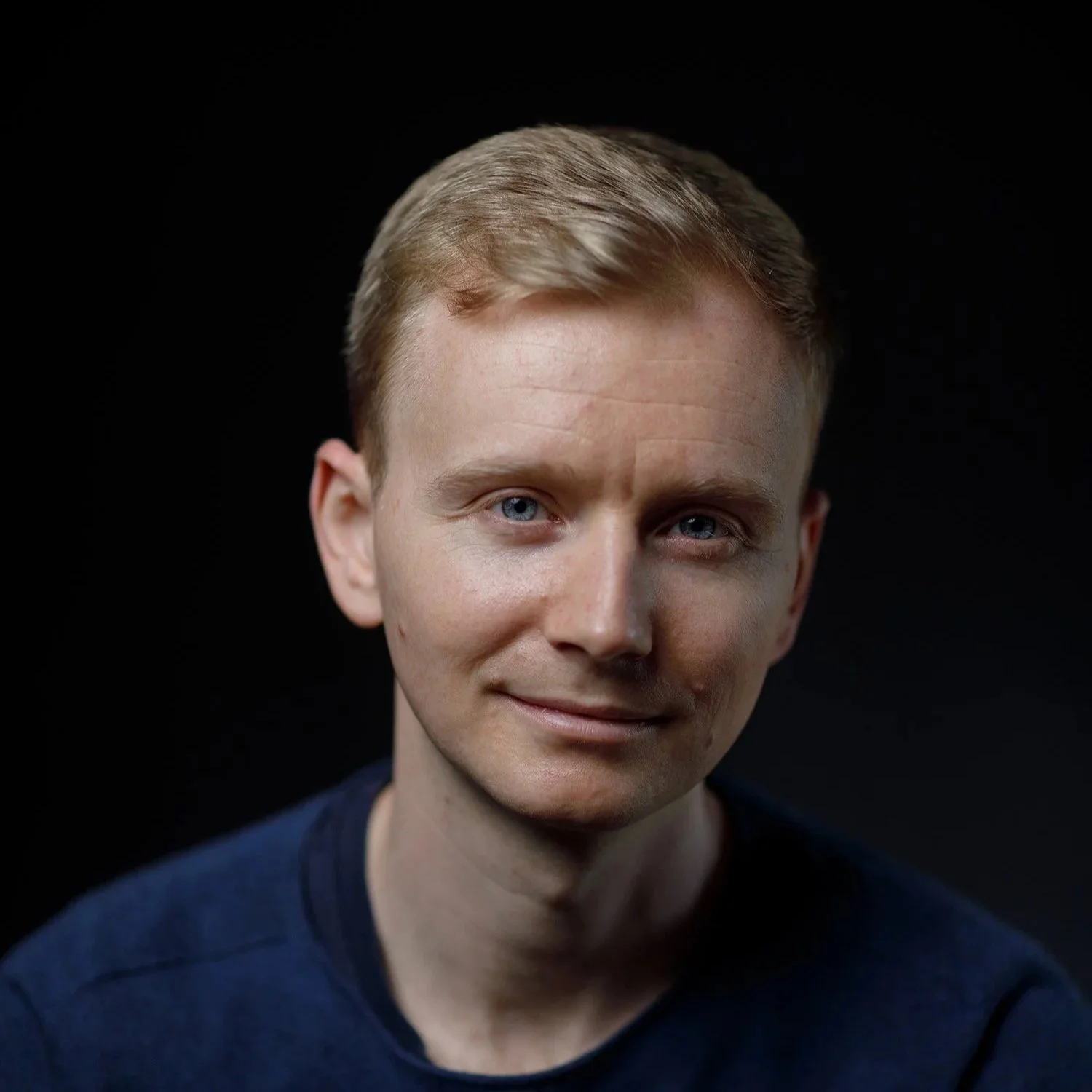 Close-up portrait of author, Andrew Wilson, wearing a dark blue shirt against a black background.