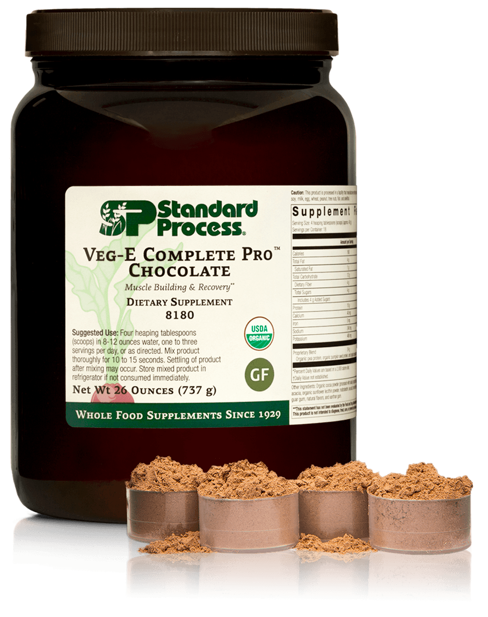 A black container of Standard Process Veg-E Complete Pro Chocolate dietary supplement with loose powder spilled in front of it