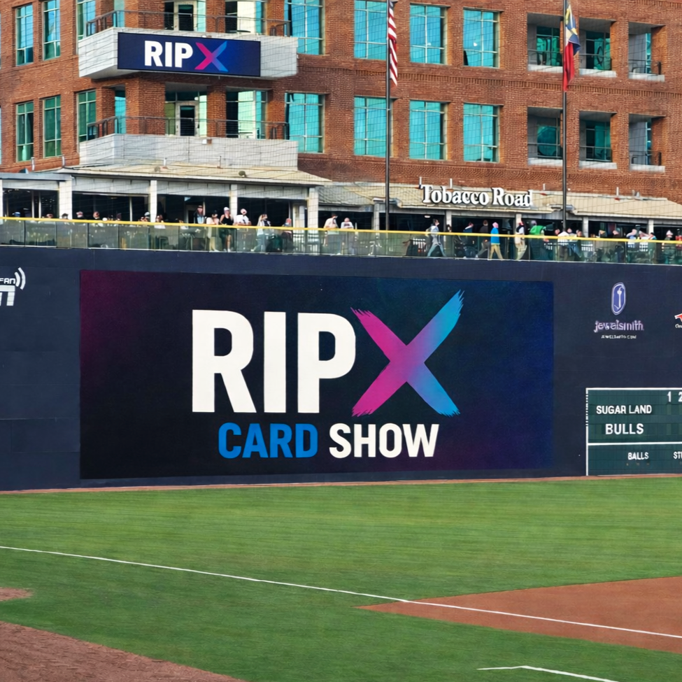View of a baseball stadium with a large digital scoreboard displaying 'RIP X Card Show'. In the background, there is a brick building with a sign that says 'Tobacco Road', flags, and spectators behind a glass railing.