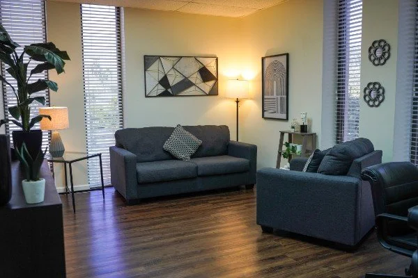 Systemic Solutions room with two gray sofas, a wooden floor, a floor lamp, decorative wall art, and large windows with blinds.