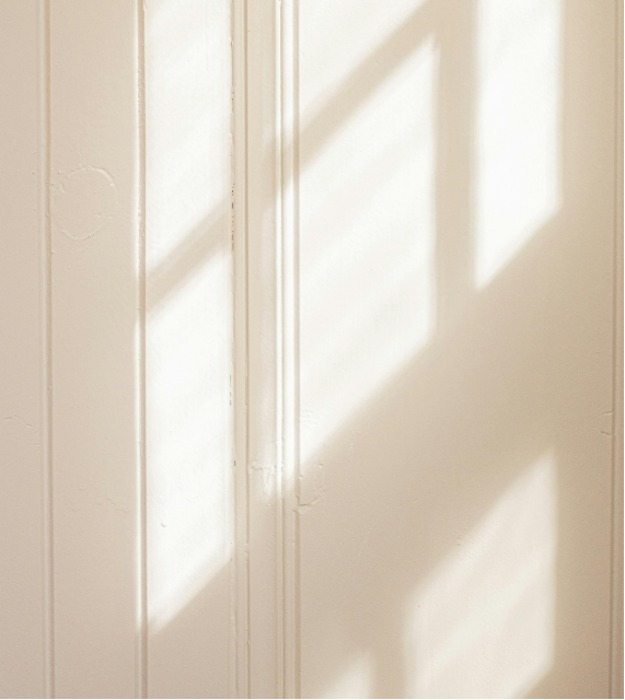 Sunlight casting shadows on a white wall near a door.