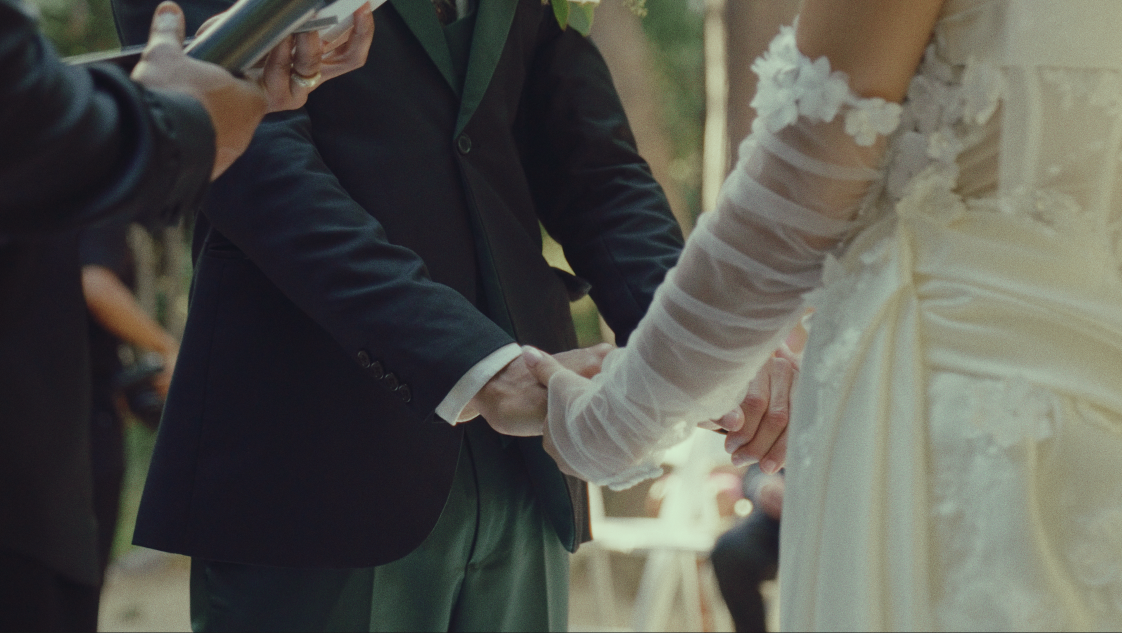 A couple holding hands during their wedding ceremony, with a person officiating and others in attendance.