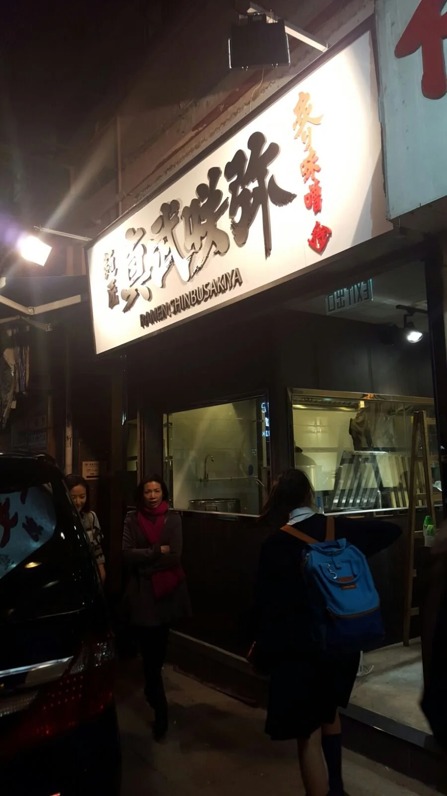 Night scene outside a restaurant with a signboard reading 'Ramen Chubu Sakuya' and Chinese or Japanese characters, with several people standing in front of it.