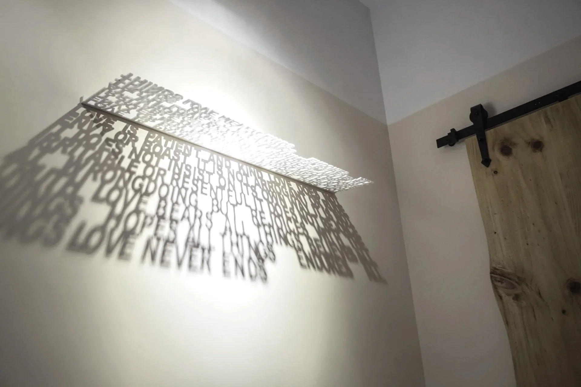 Shadow of a decorative wall art with words cast on a wall next to a sliding barn door.