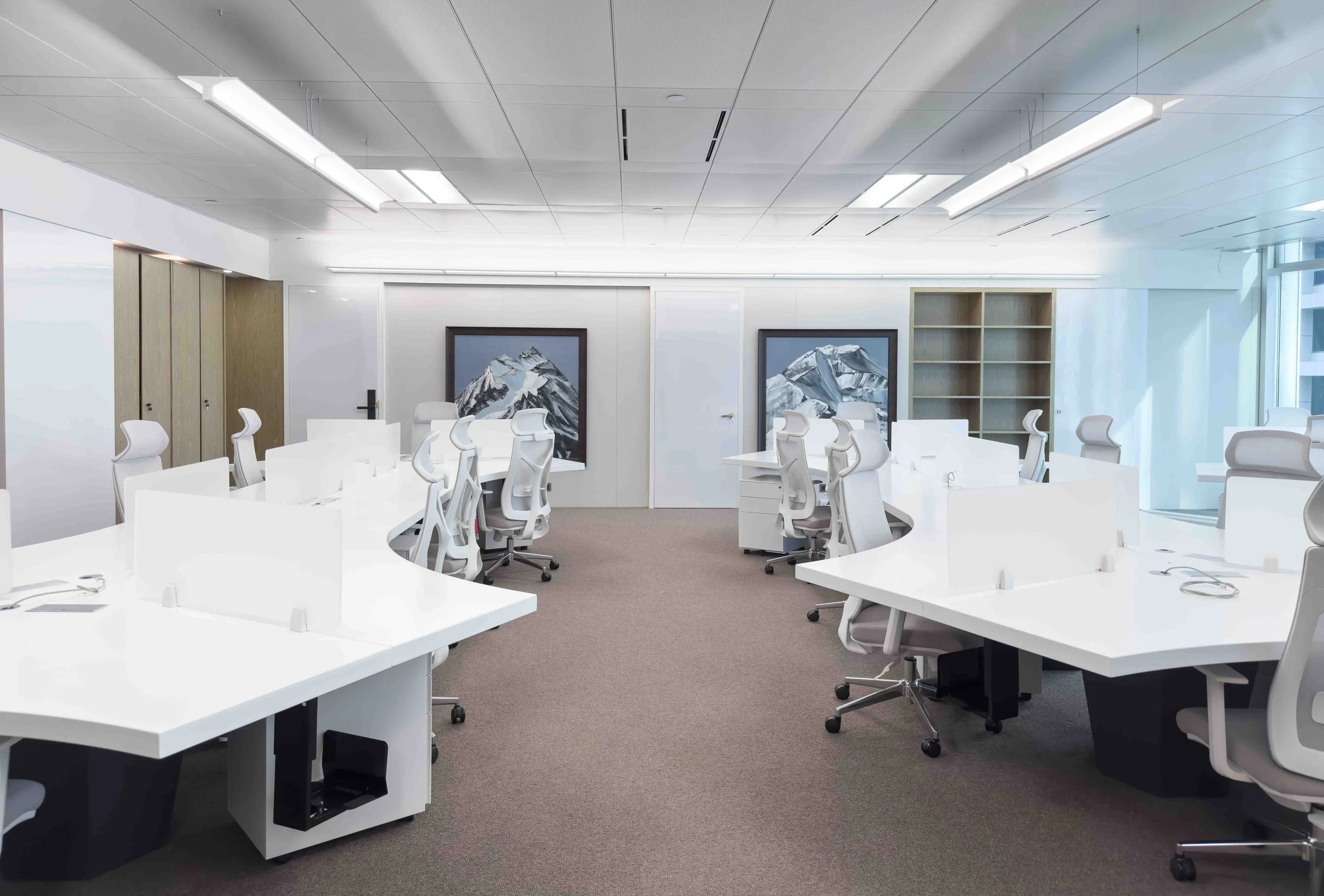 Empty modern conference room with white desks, ergonomic chairs, and artwork of mountains on the walls.