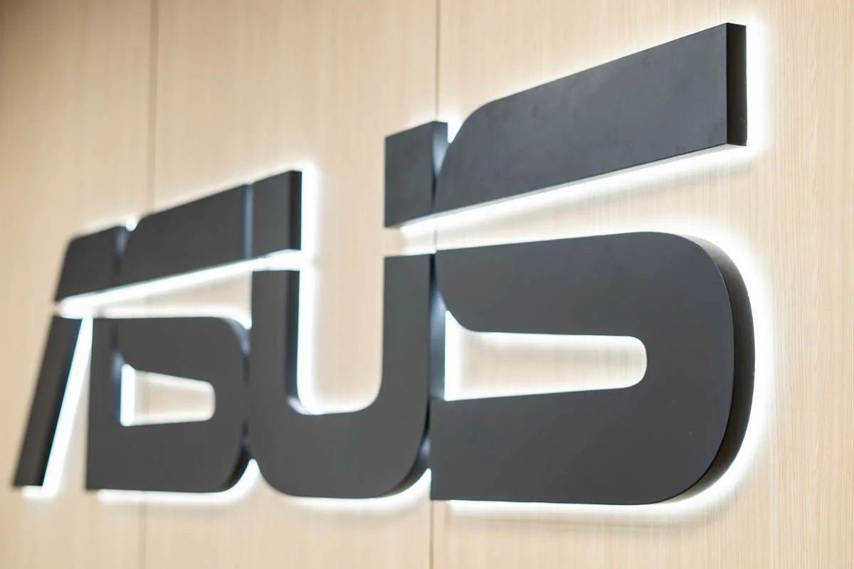 Close-up of a black 3D company logo on a light wooden wall, with backlit lighting highlighting the logo's edges.