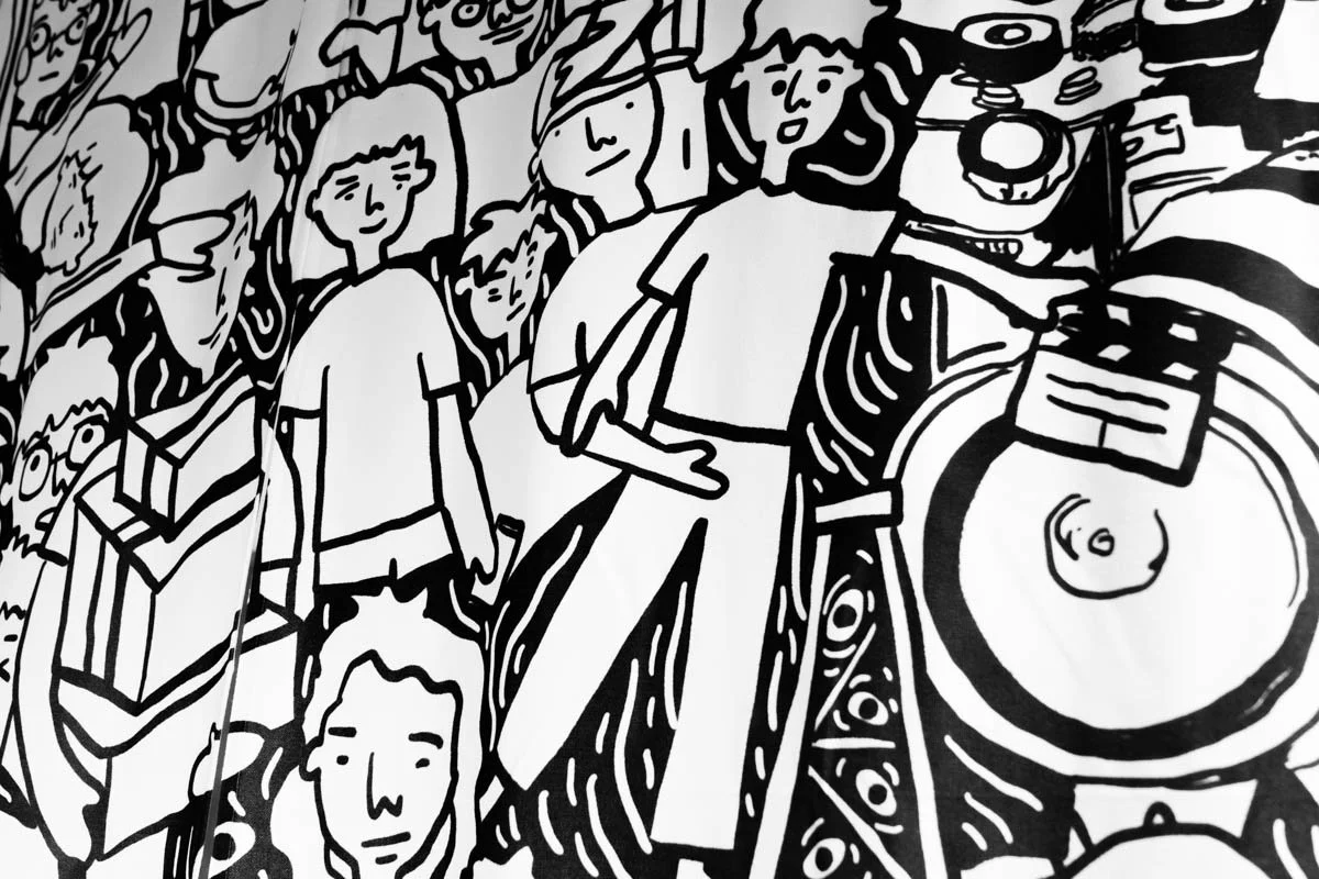 Black and white cartoon illustration of a group of people dancing and enjoying music at a party or club, with a DJ playing on turntables.