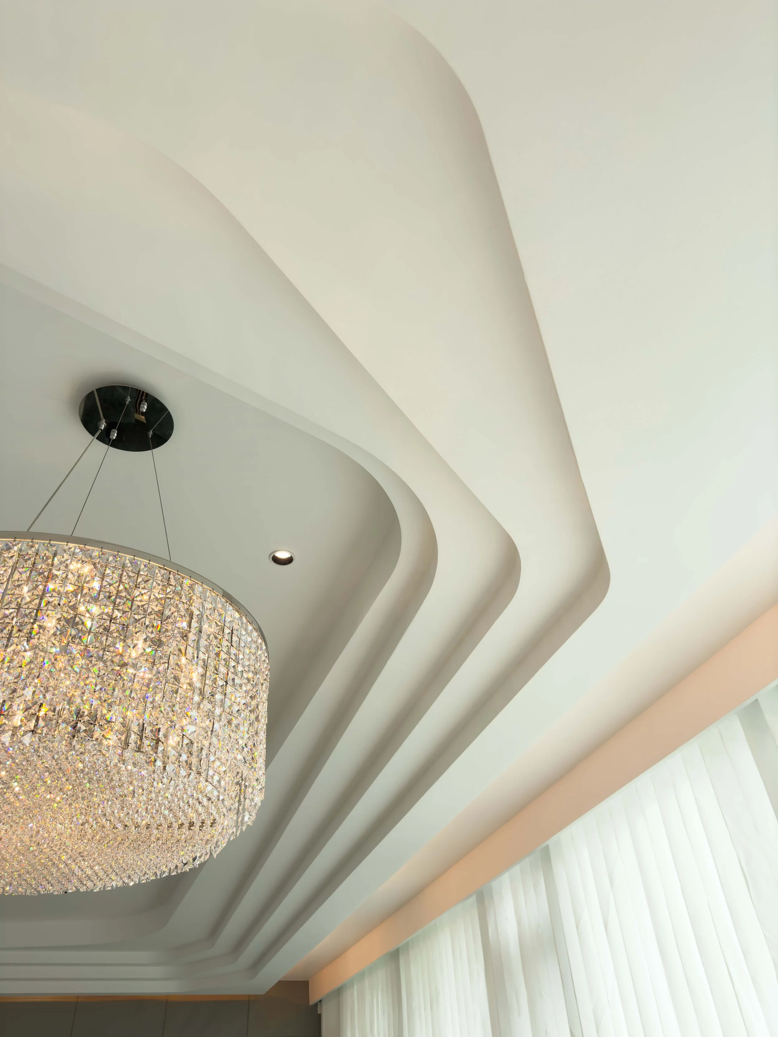 Elegant ceiling with layered design and a large crystal chandelier in a modern room.