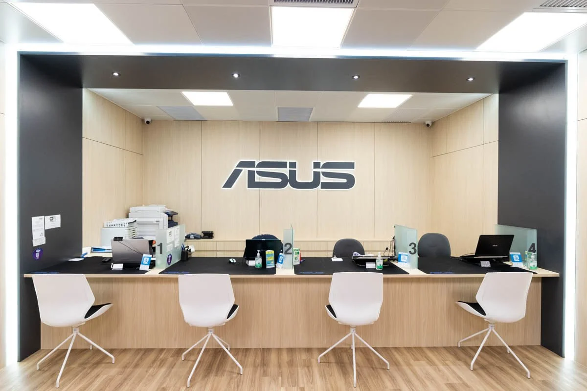ASUS customer service counter with four chairs, computers, and dividers in a modern office setting.