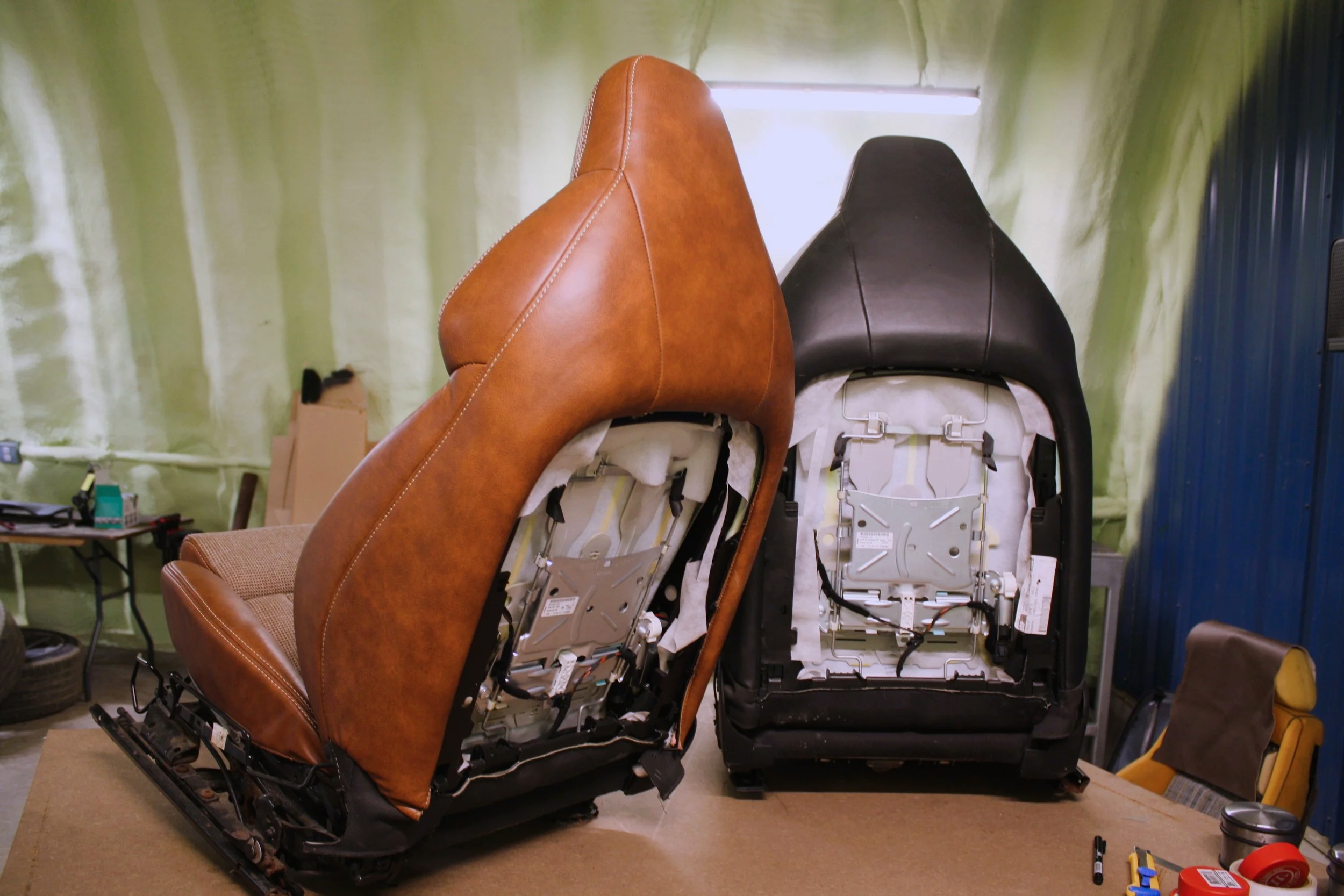 Two car seats with their covers removed, showing internal mechanisms, placed on a workbench in a workshop.