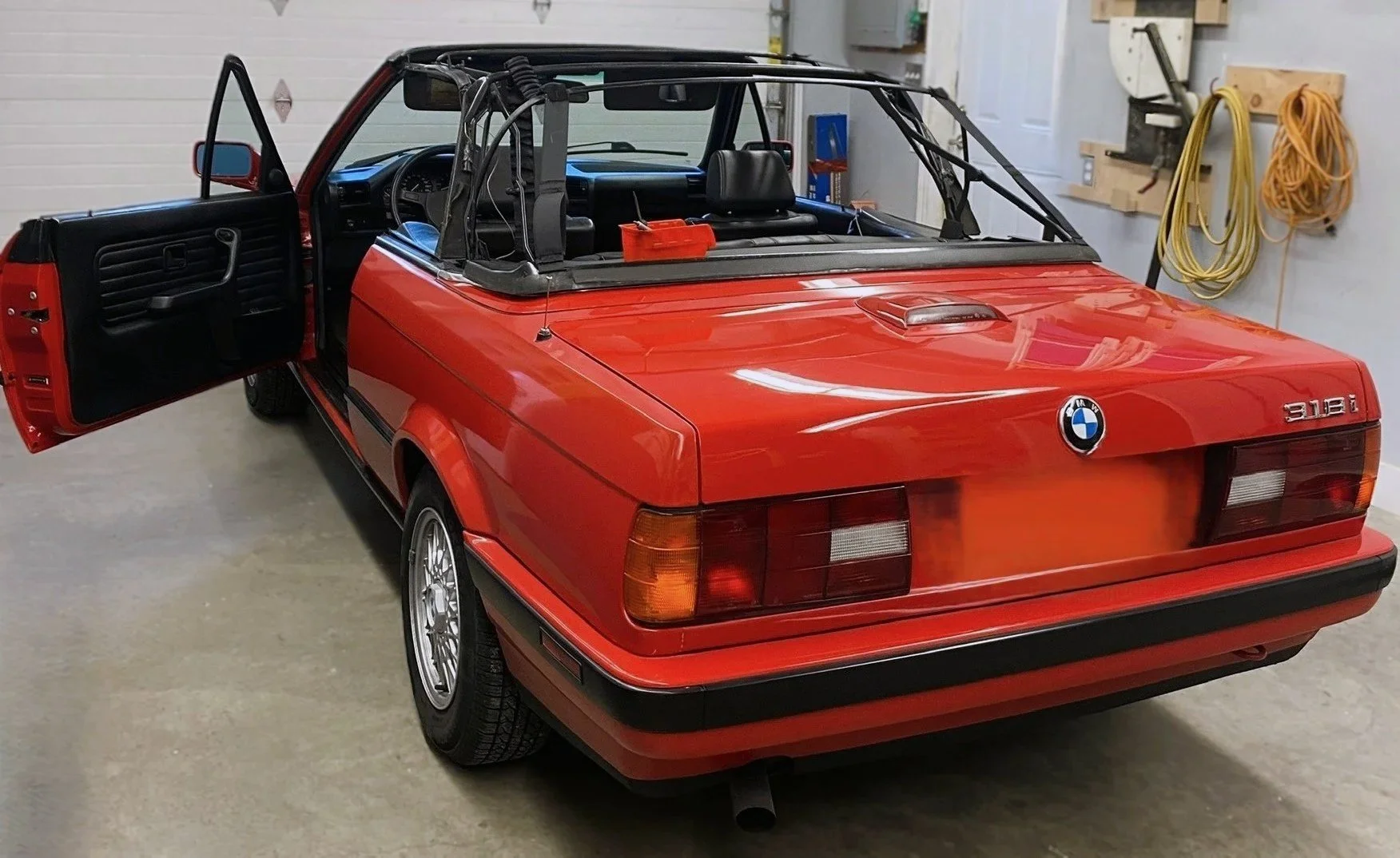 Red BMW 3 Series convertible car with open driver's side door inside a garage.