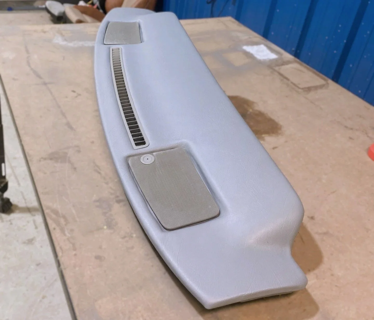 Automotive dashboard with air vent, speaker, and a sensor or switch, placed on a wooden surface.