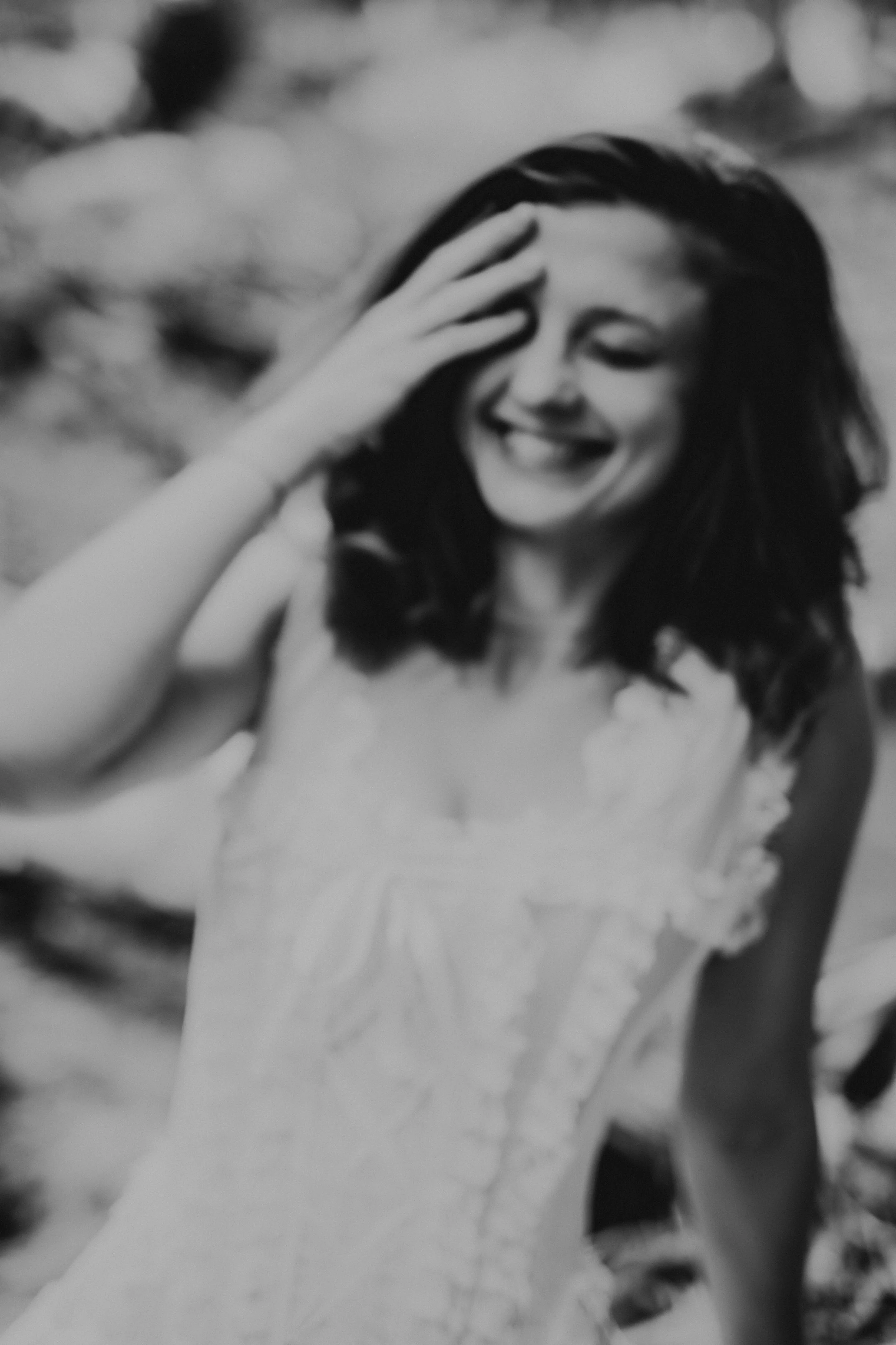 Black and white photo of a woman smiling and laughing, with her hand on her forehead, outdoors with rocks in the background.
