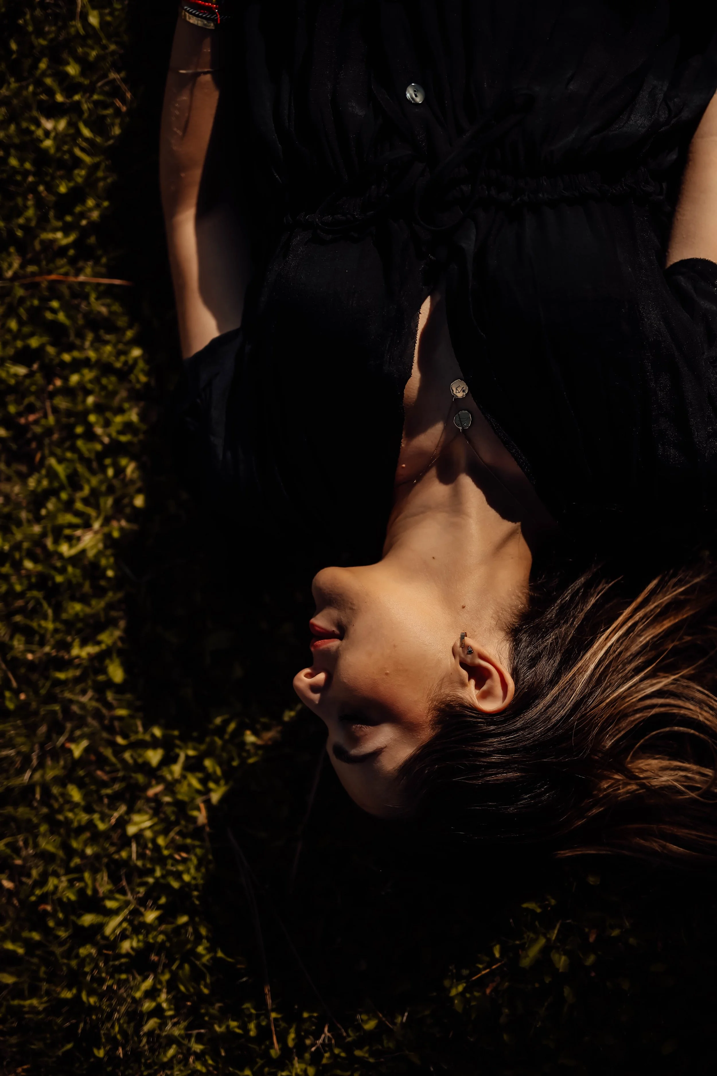 A woman with dark hair lying on a bed of grass with her head turned to the side.
