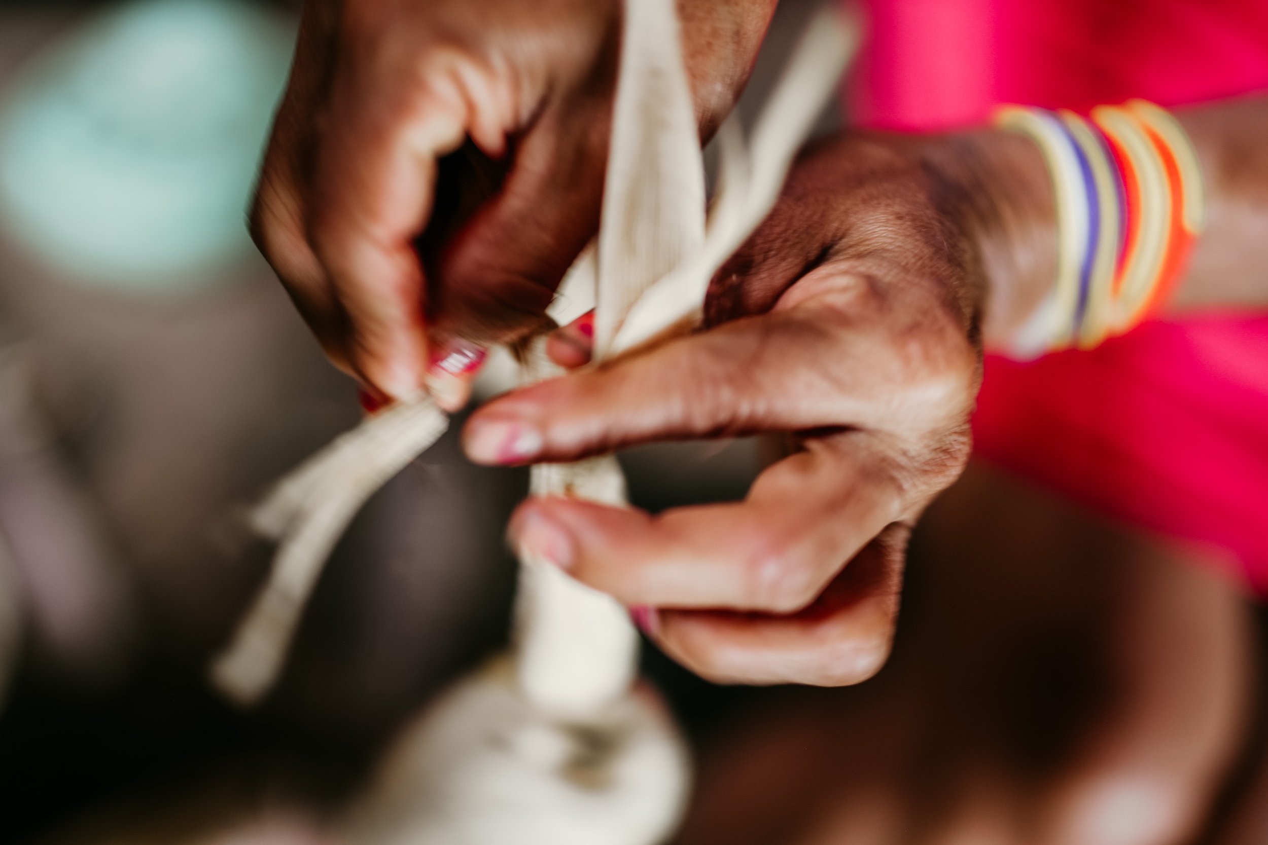 Close-up of hands tying a rope, with colorful bangles on the wrist, wearing a pink garment.