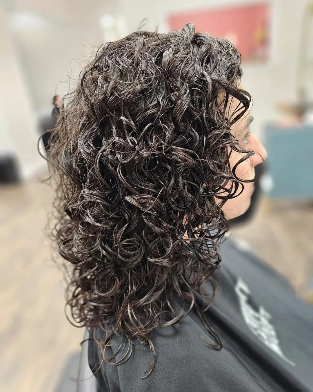 Woman with shoulder-length, dark, curly hair at a salon.
