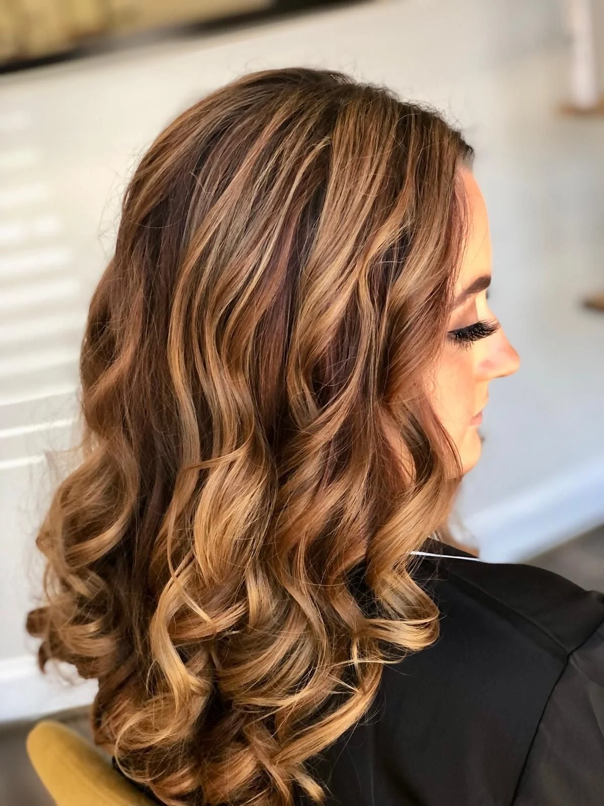Side profile of a woman with long, wavy, light brown hair with highlights, wearing a black top.