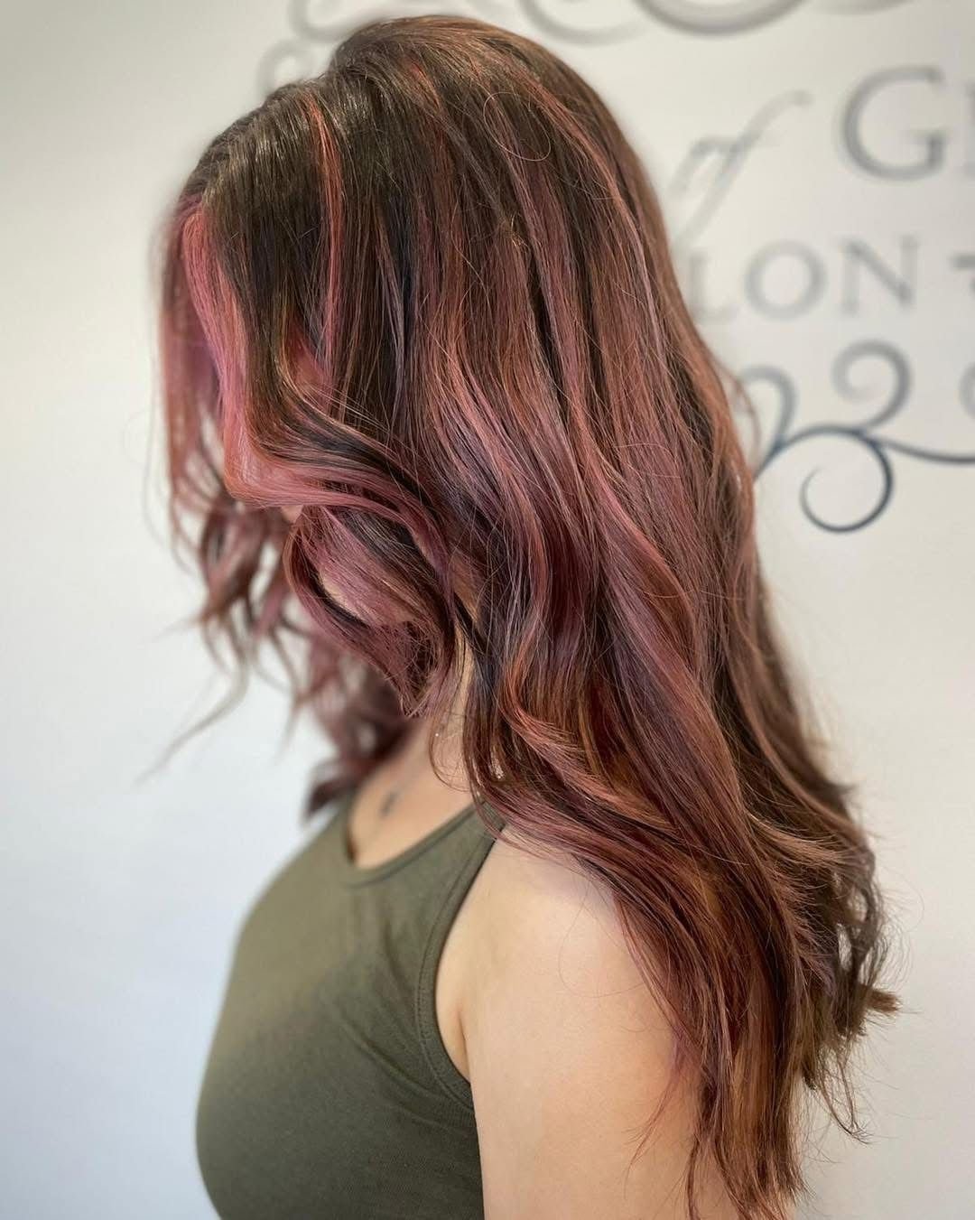 Side view of a woman with shoulder-length wavy rose gold hair, wearing a dark green sleeveless top.