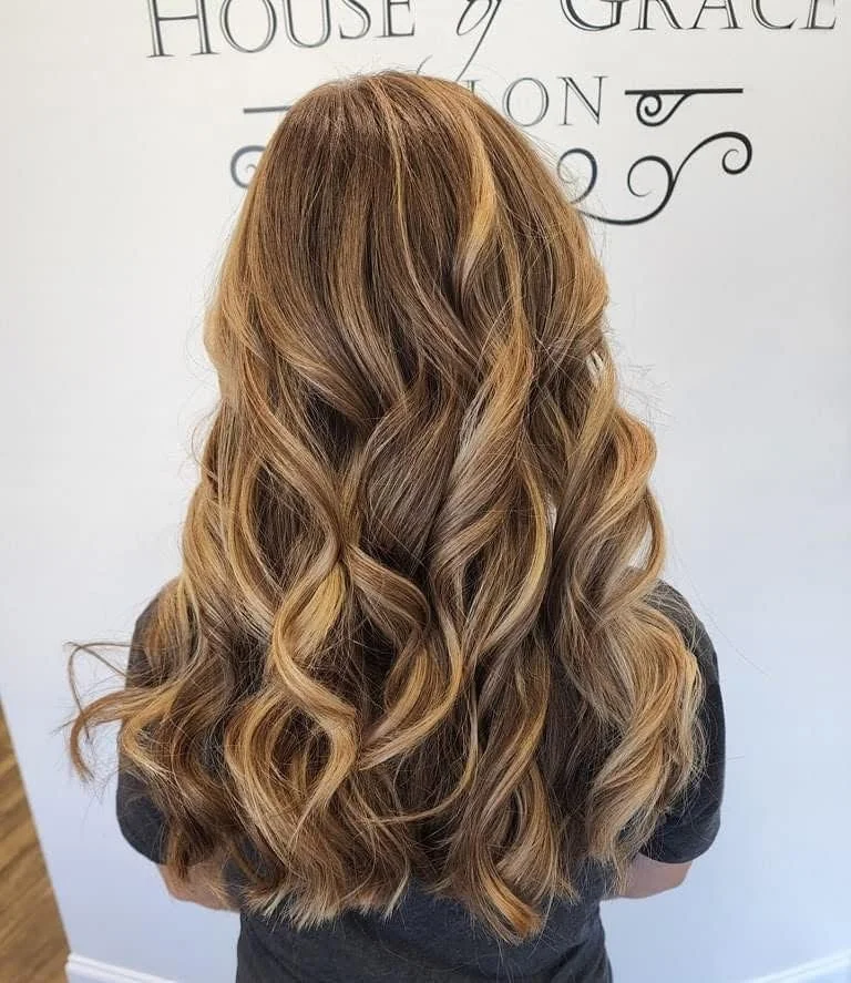 Back view of a woman with long, wavy, caramel-colored hair against a white wall with text.