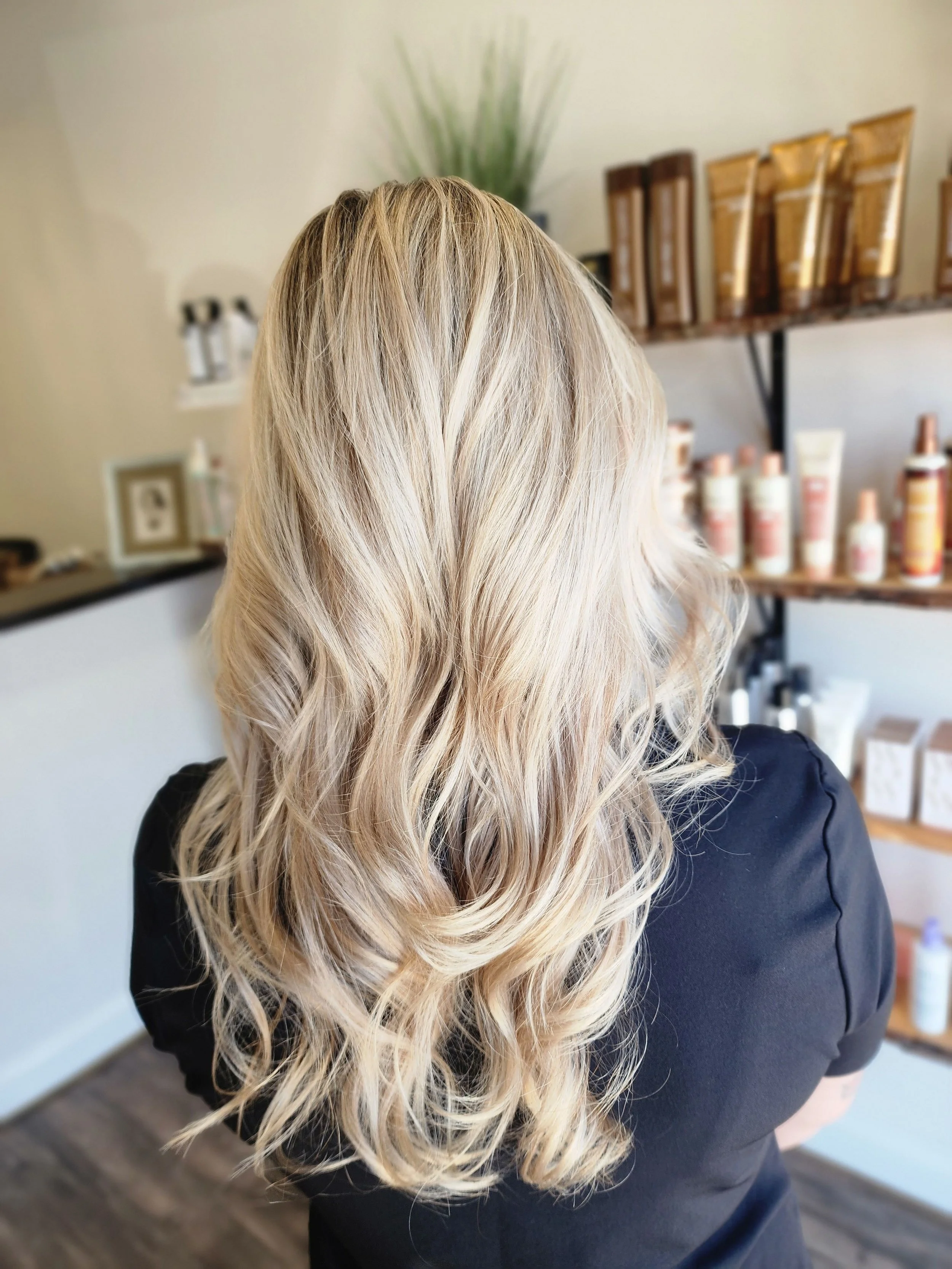 Woman with long, wavy blonde hair in a salon or similar setting.
