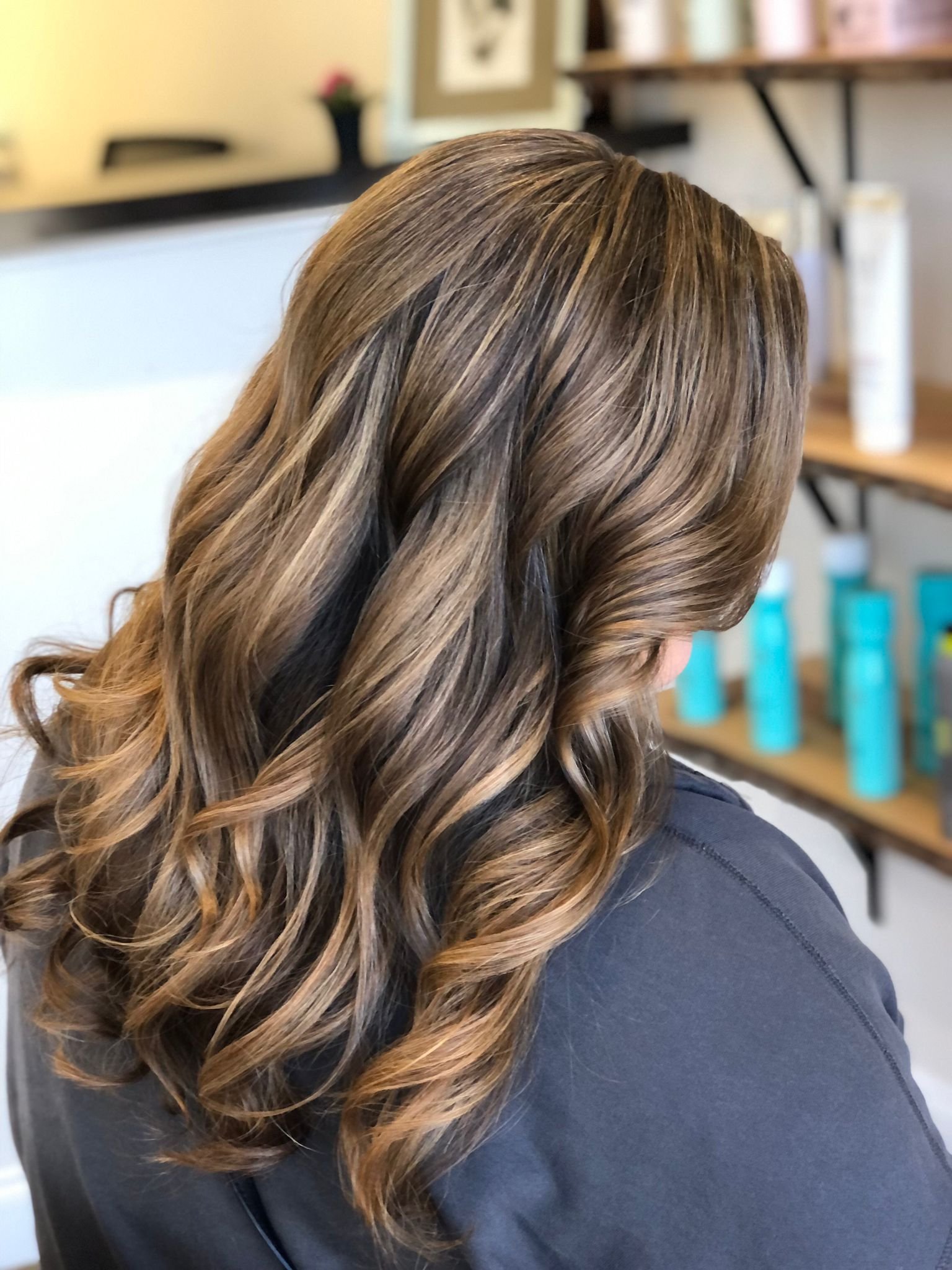 Woman with styled, wavy brown hair with blonde highlights in a salon setting.