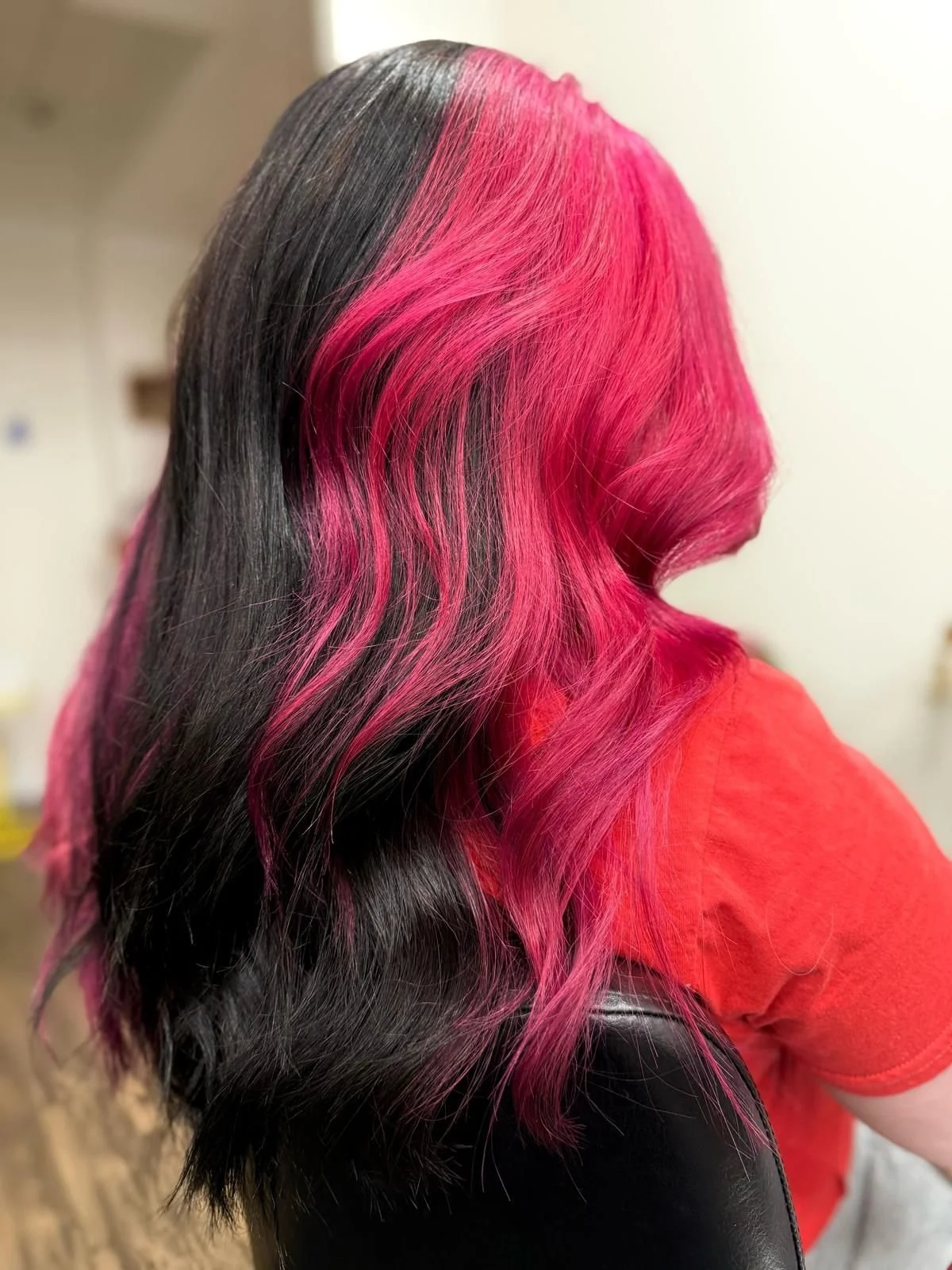 A person with long, black hair dyed bright pink on top, styled in loose waves.