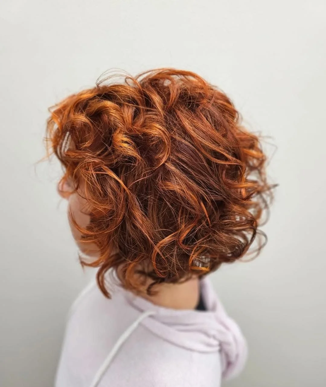 Close-up of a person's head with short, wavy, bright red hair.