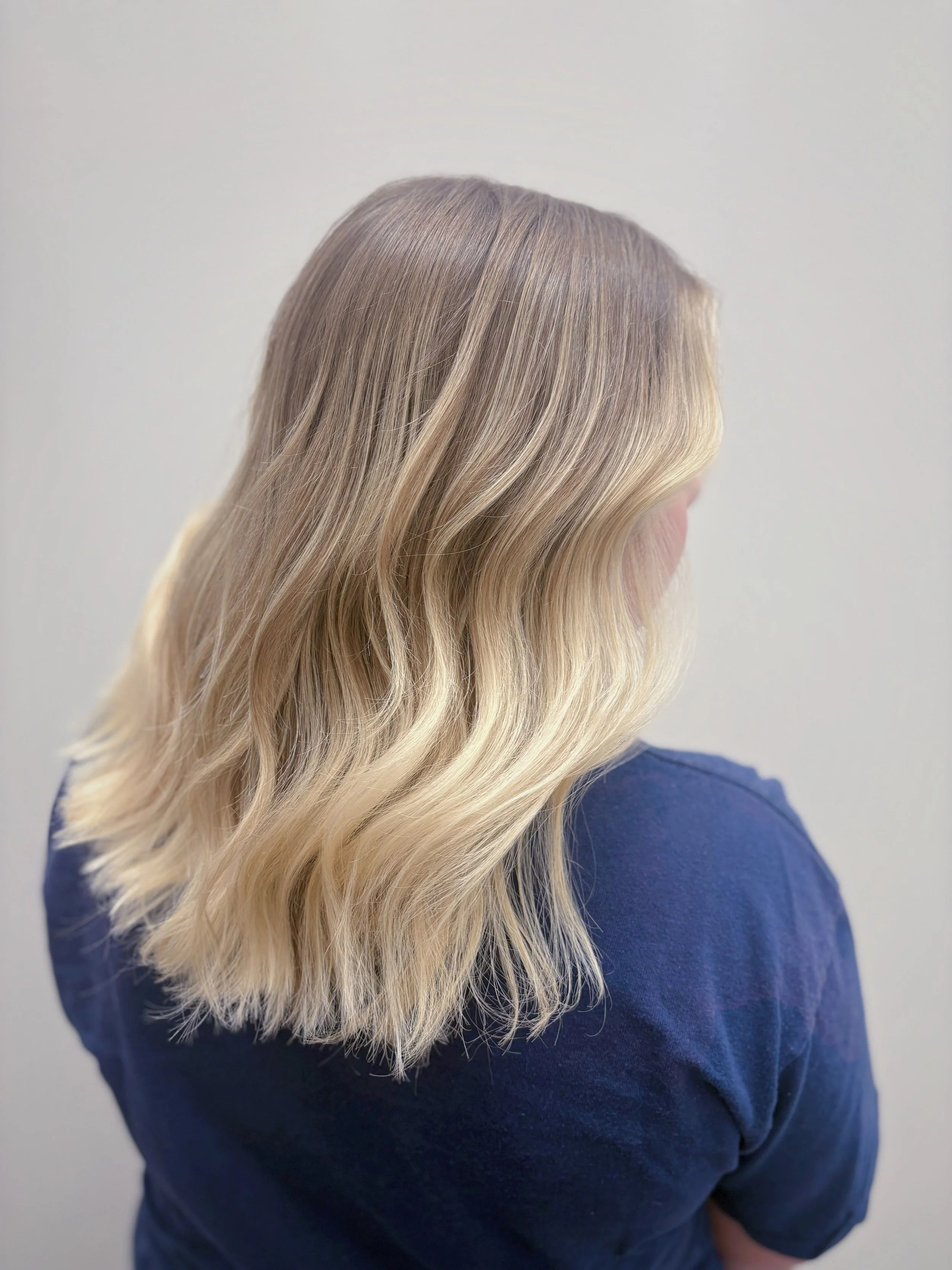 Side view of a woman with long, wavy blonde hair wearing a blue sweater.