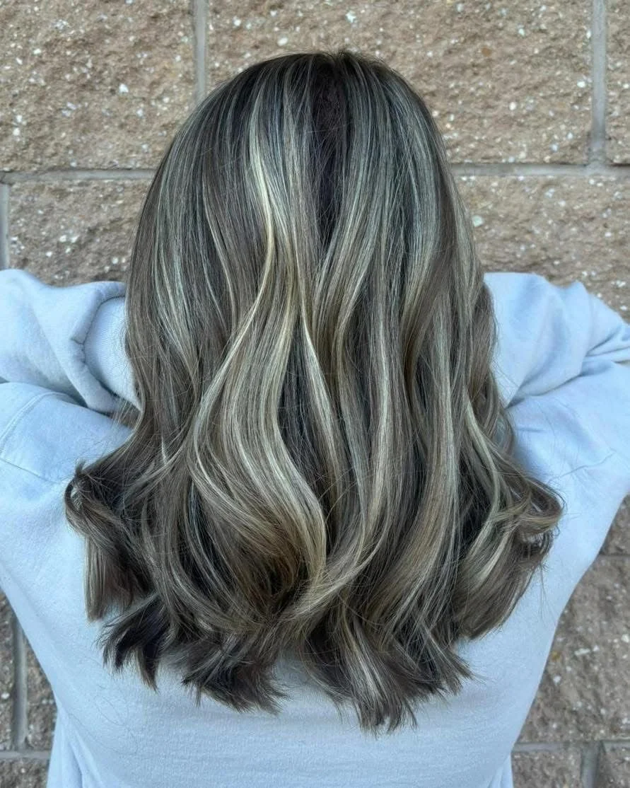 Back view of a person's head showing long, wavy, blonde-highlighted hair against a brick wall background.