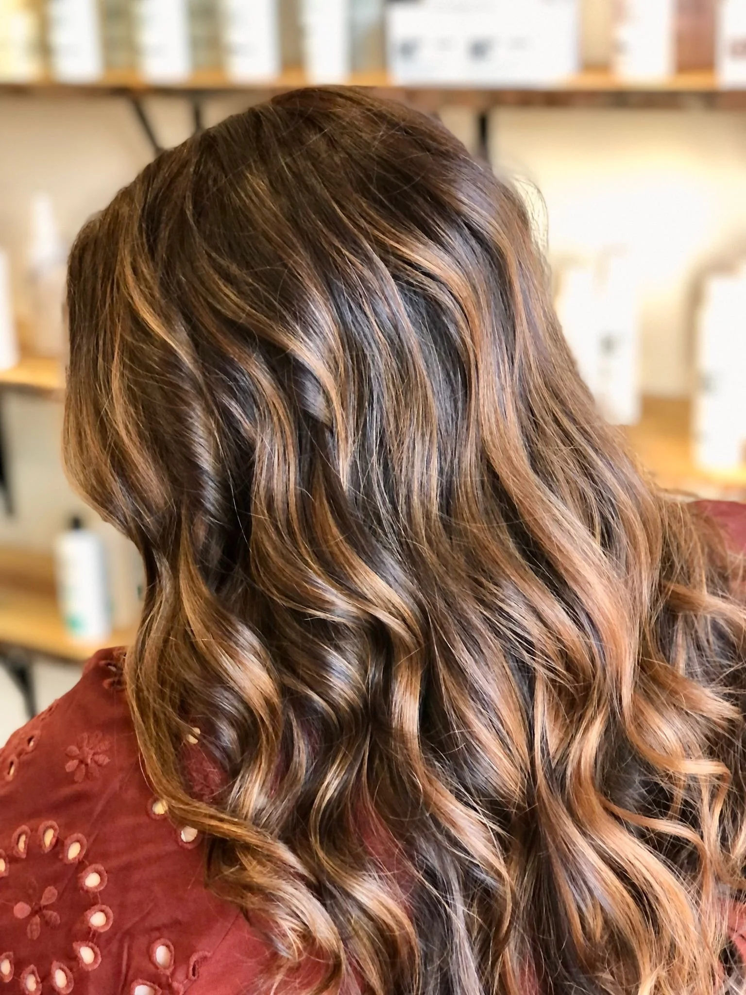 Close-up of a person's wavy, brown hair with subtle highlights, styled in loose curls, in a salon setting.