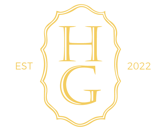 A logo with a black background, featuring a gold ornate frame and the letters H and G in the center. The words "EST" and "2022" are on the sides of the frame.